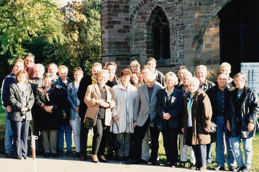 Historisches Gruppenfoto: eine große Gruppe Erwachsener steht vor einer Kirche aus Bruchstein