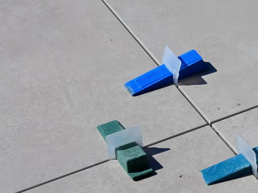 Nivellierclips und Fliesenkeile in den Fugen frisch verlegter grauer Bodenfliesen