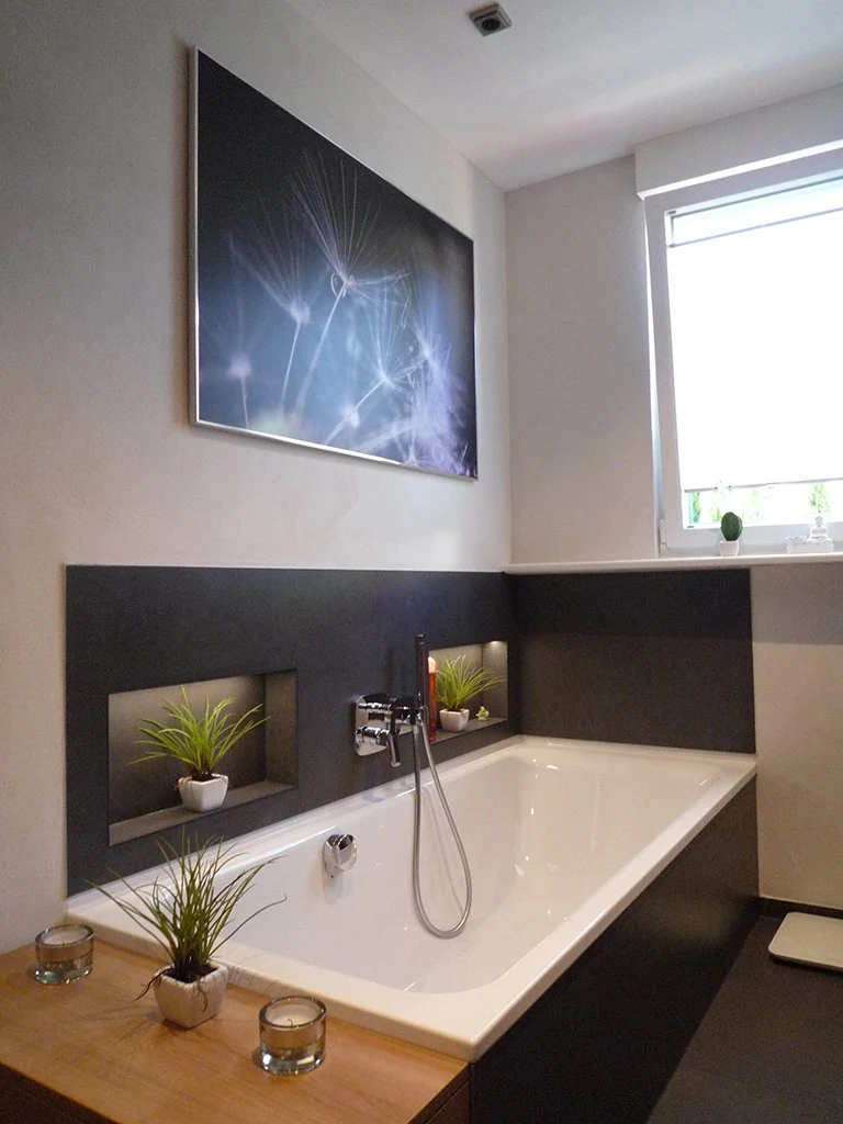 Badewanne vor einer dunkel gefliesten Vorwand mit zwei beleuchteten Nischen, daneben ein Fenster